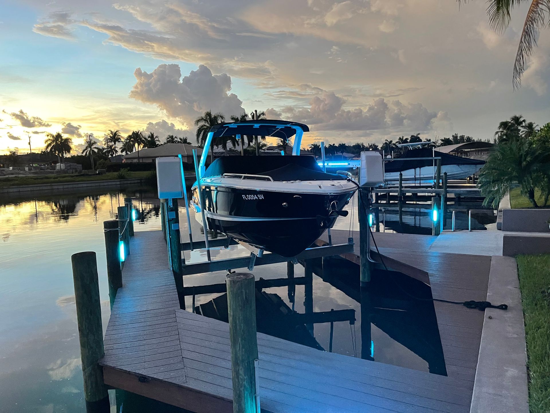Boat on a dock at dusk, reflected in the water; illuminated by blue lights.