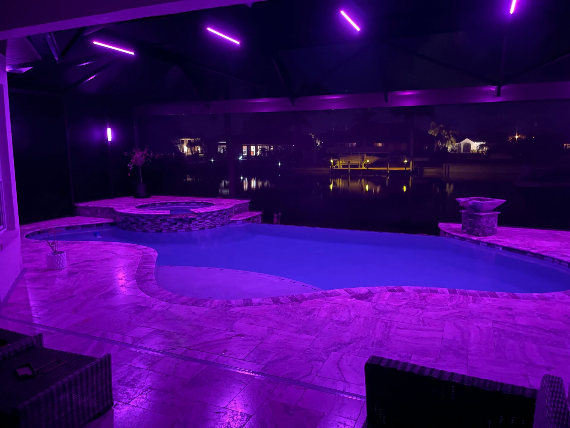 Pool area at night illuminated with purple lights, overlooking a lake.