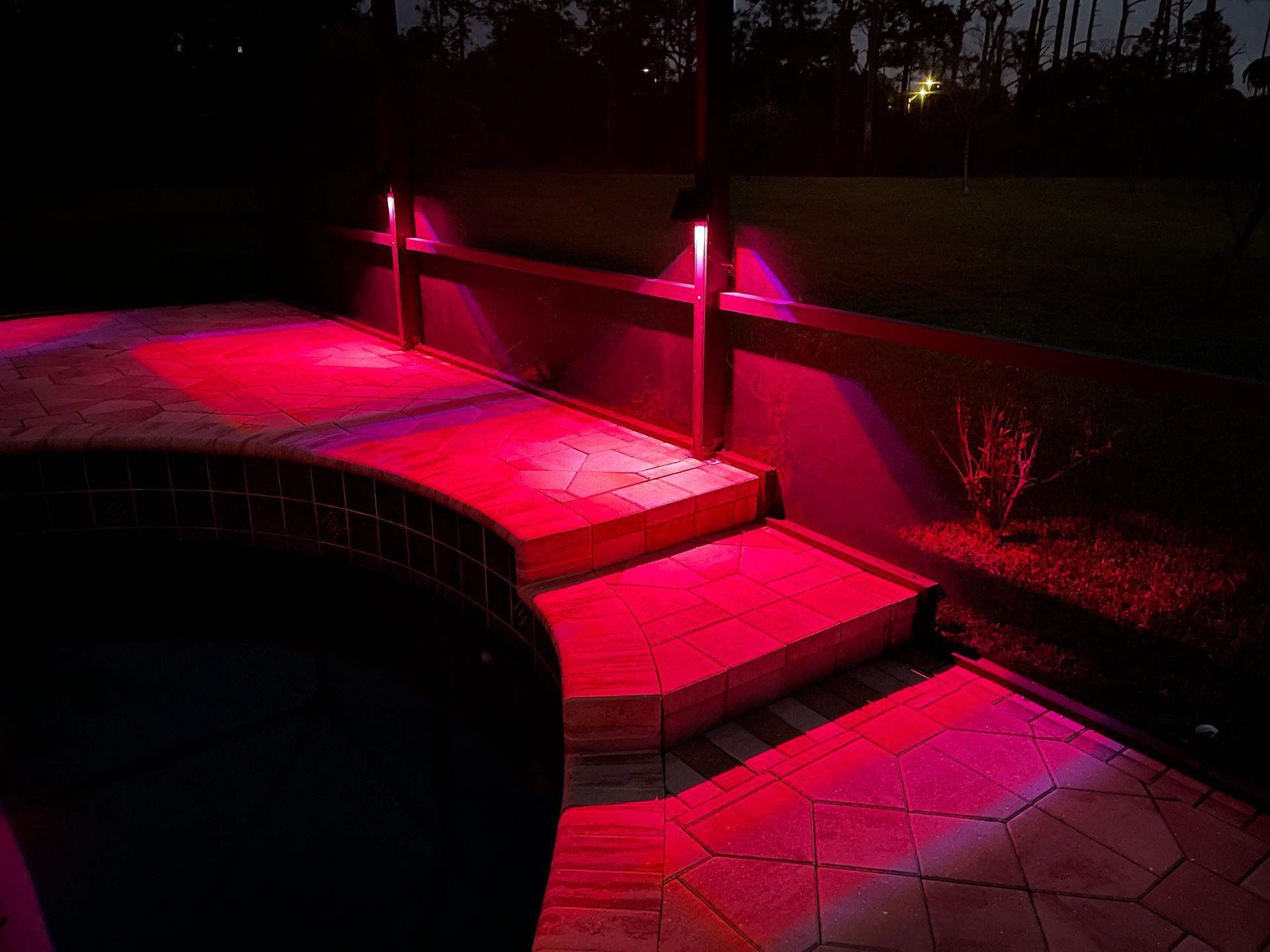 Red outdoor lighting illuminates a stone patio, steps, and wall at night.