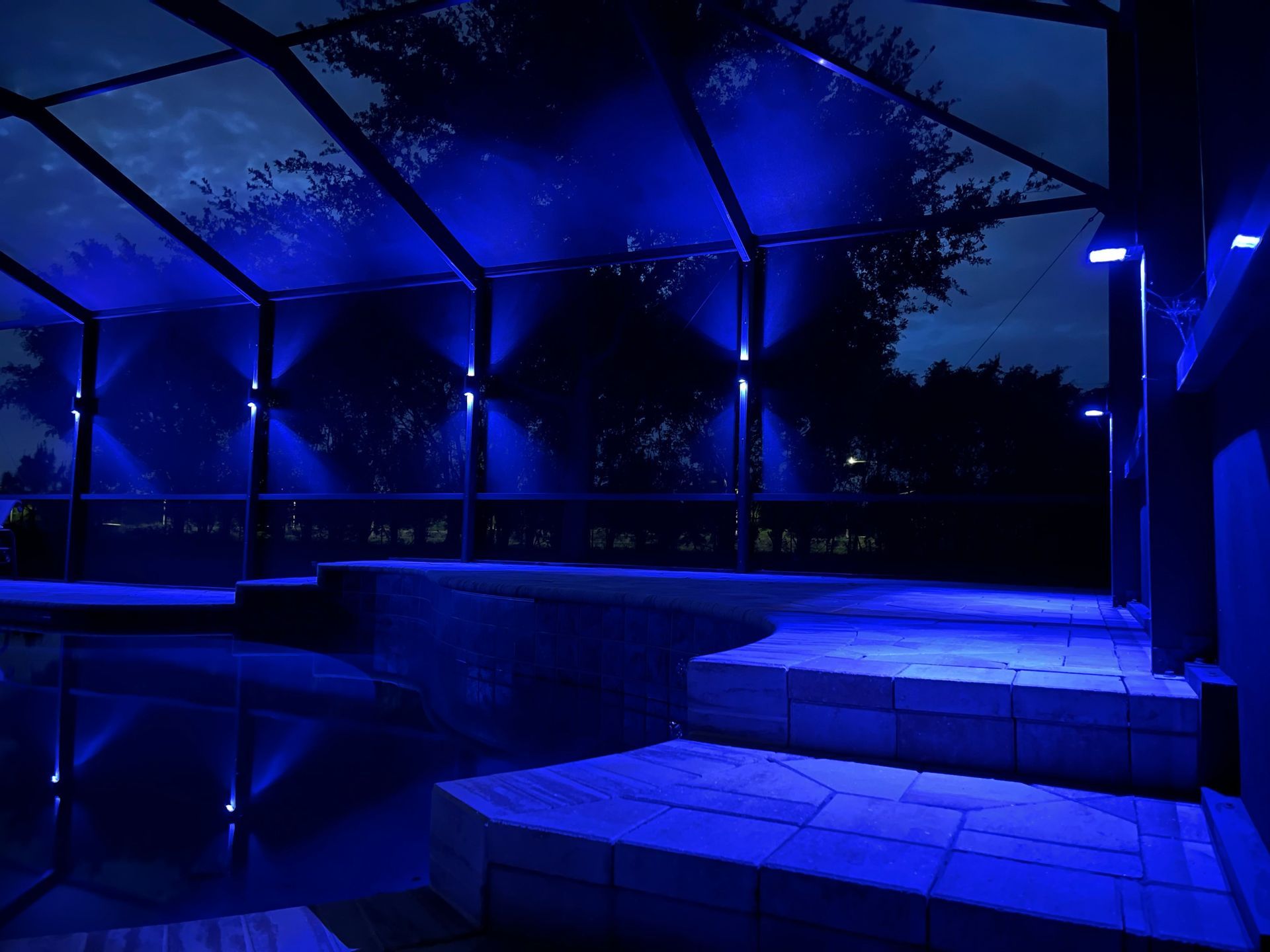 Blue-lit outdoor patio at night, with a pool and pergola.