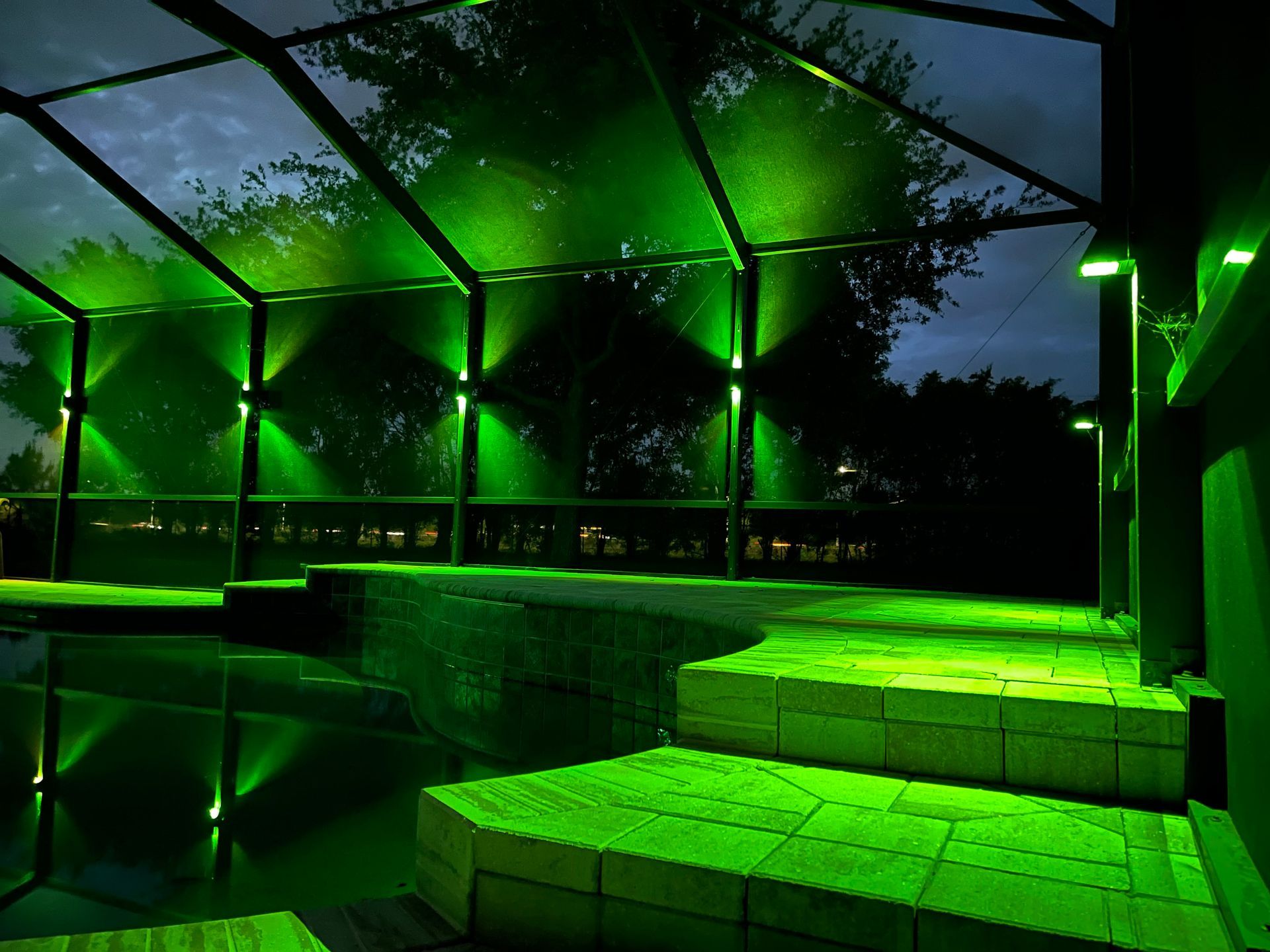 Green-lit outdoor structure, steps lead to a pool, dark night sky with tree silhouettes.