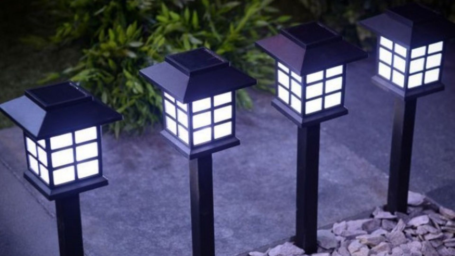 Four black solar-powered garden lights illuminating a stone pathway at dusk.