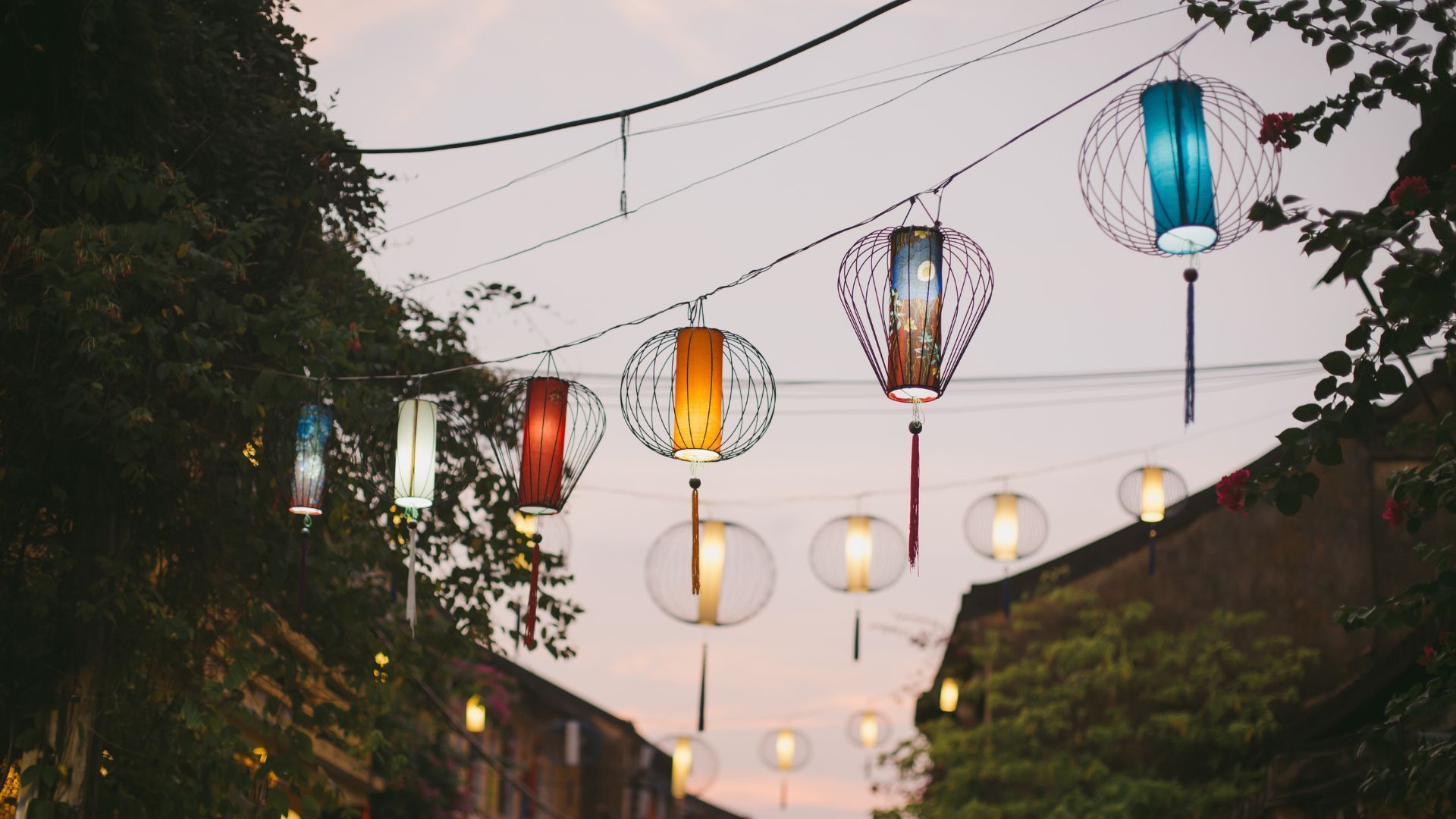 String of colorful lanterns strung across a street at dusk.