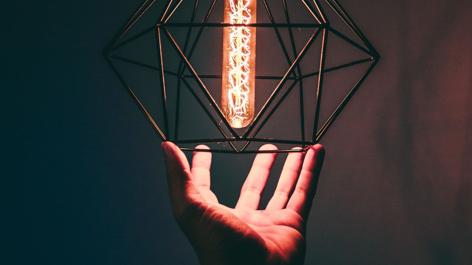 Hand holding geometric wireframe lamp with illuminated filament.