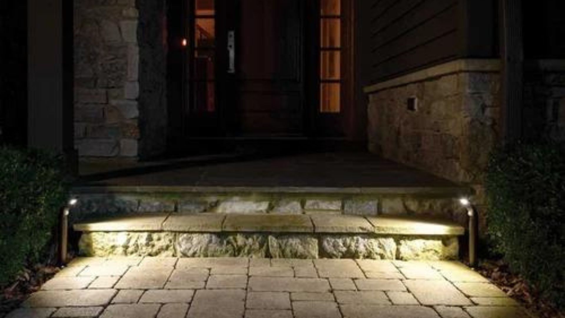 Stone steps lit by ground lights leading to a dark wooden door.