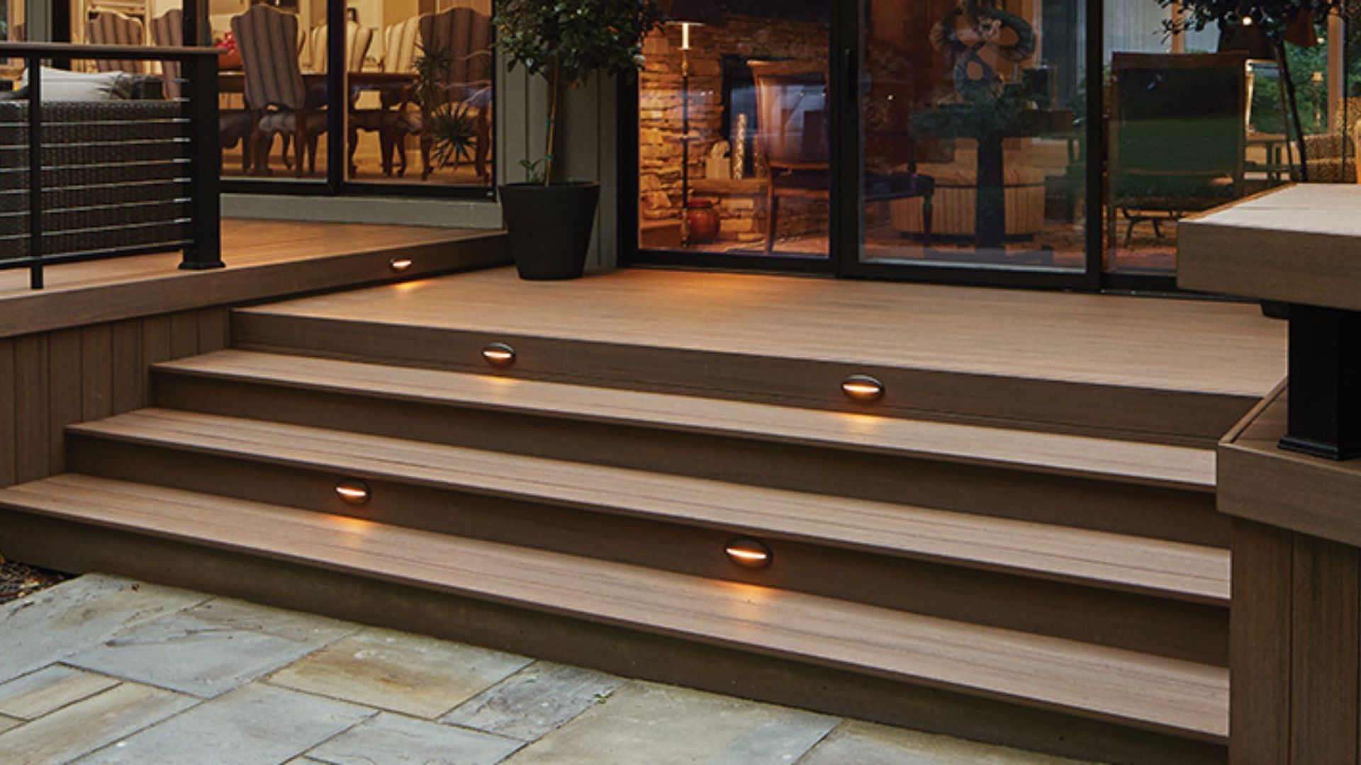Wooden deck with steps illuminated by small lights, leading to a glass door.