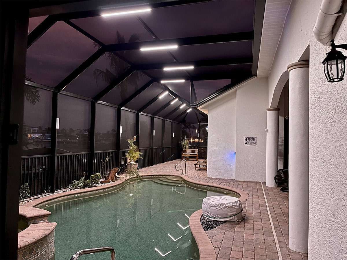 Enclosed pool area with dark screen, interior lights, brick patio, and steps leading to pool.