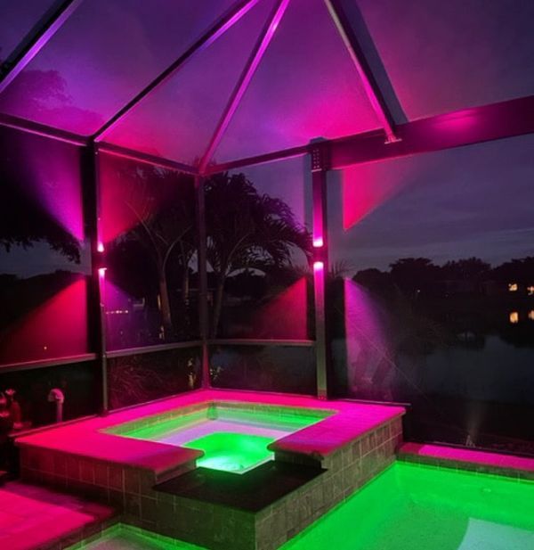 Screened-in patio with table and chairs, illuminated by overhead and wall lights at night.