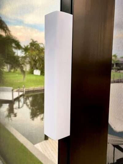 White rectangular light fixture mounted on a dark brown column, next to a window with a waterfront view.
