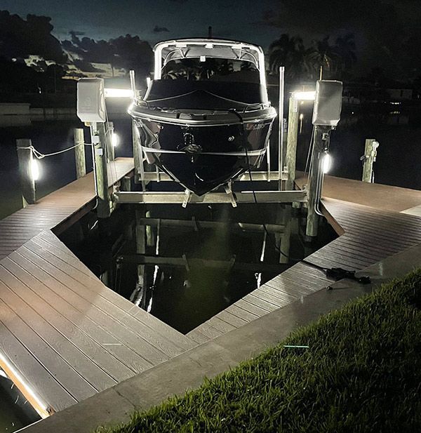 Boat docked on a lift at night. The boat is dark against the lit dock.