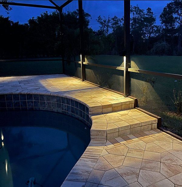 Nighttime patio with pool; stone steps and deck lit by wall-mounted lights.