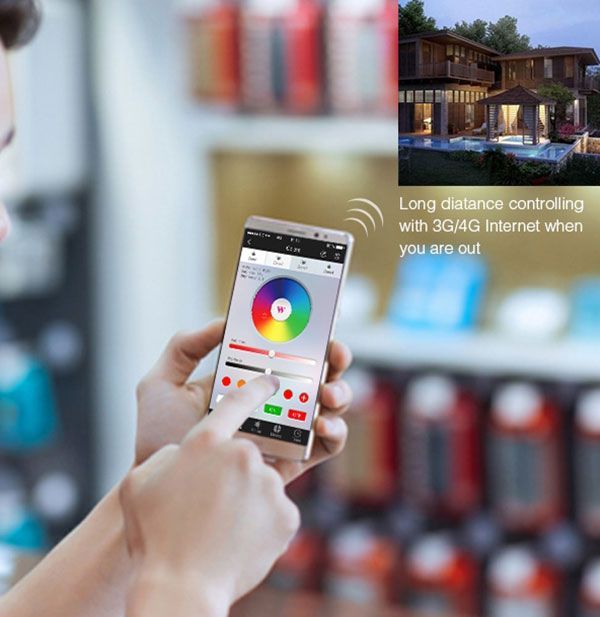Person holding a smartphone controls house lights remotely. App interface shows color wheel. House illustration inset.