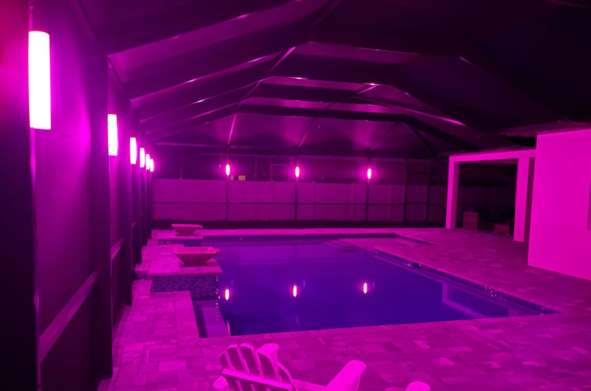 Purple-lit indoor swimming pool. Rectangular pool, dark walls, overhead canopy, vertical lights.