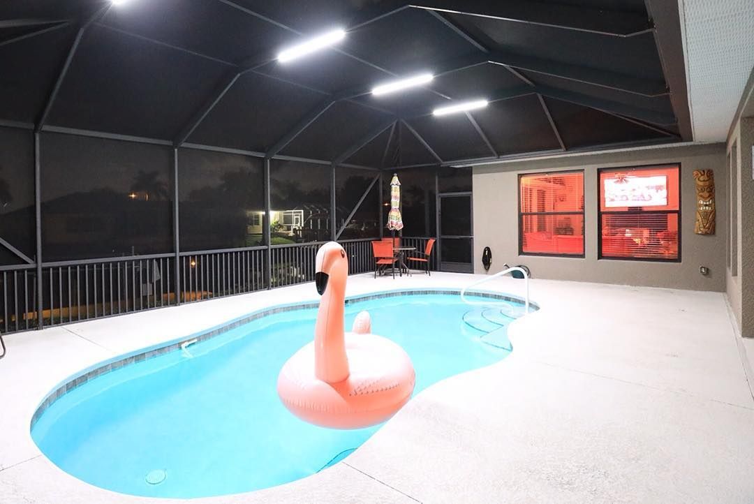 Indoor pool with pink flamingo floatie, under a screened enclosure, lit at night.
