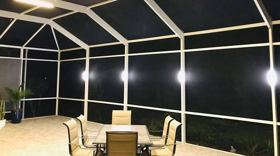 Outdoor patio enclosed by white screens, illuminated by overhead lights. Dining table with chairs visible.