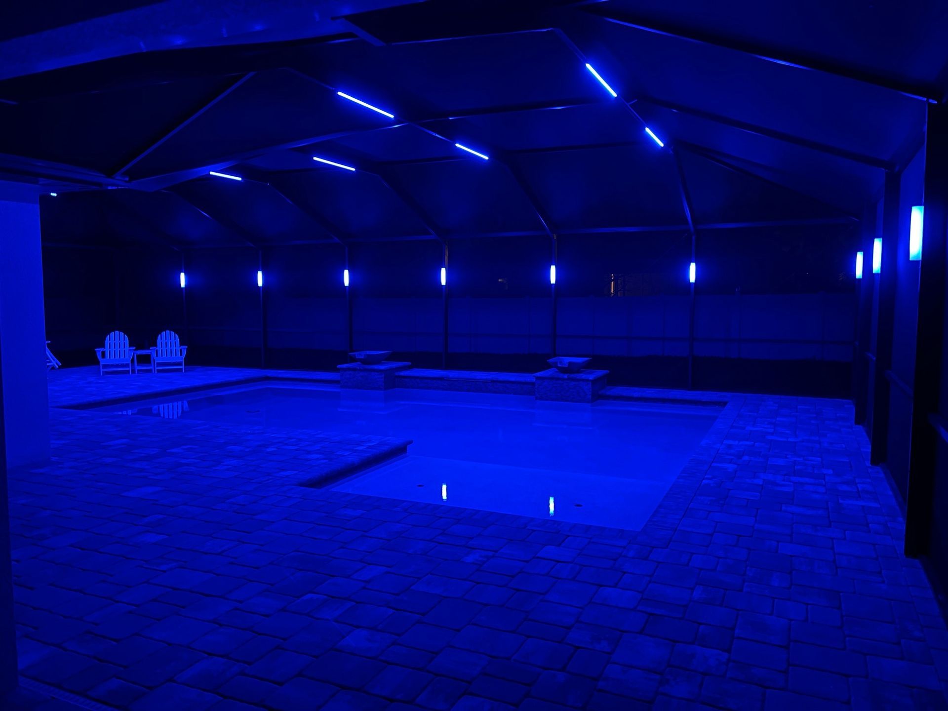 Blue-lit indoor pool area with pool and roof, illuminated by blue lights. Two chairs visible.