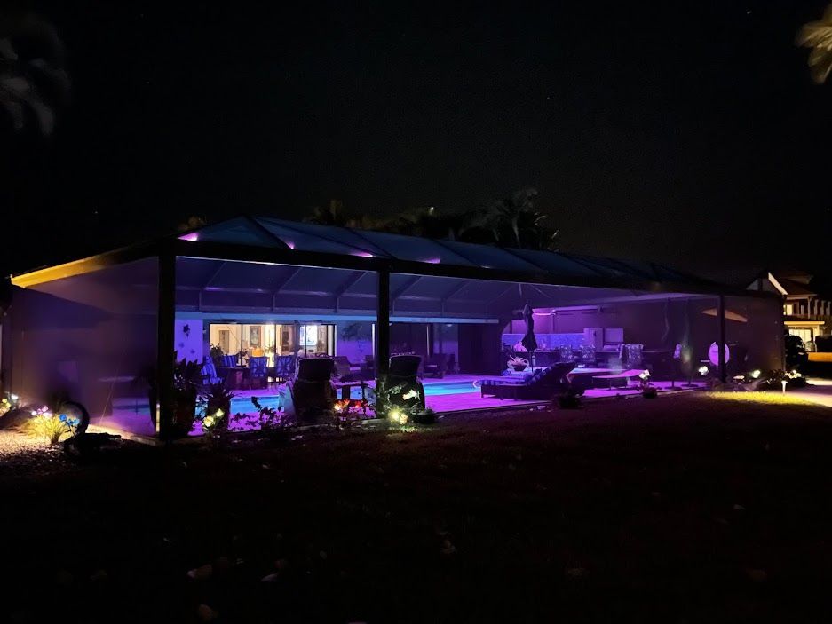 Night scene of a lit pool area with blue and purple lights, under a screened enclosure.