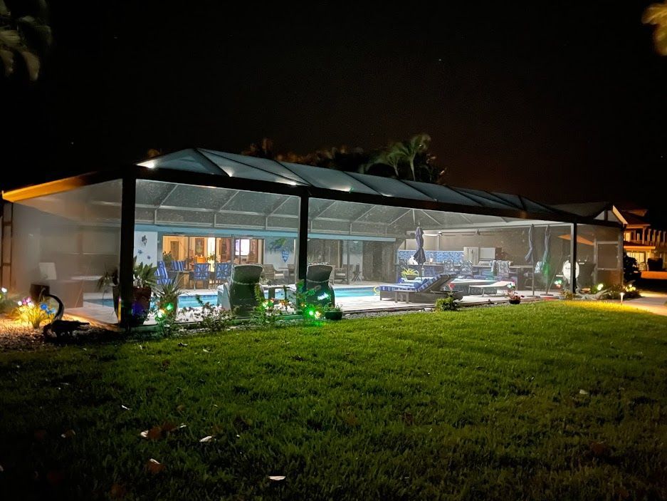 Night view of a screened-in pool area with lit interior, pool, and lawn.