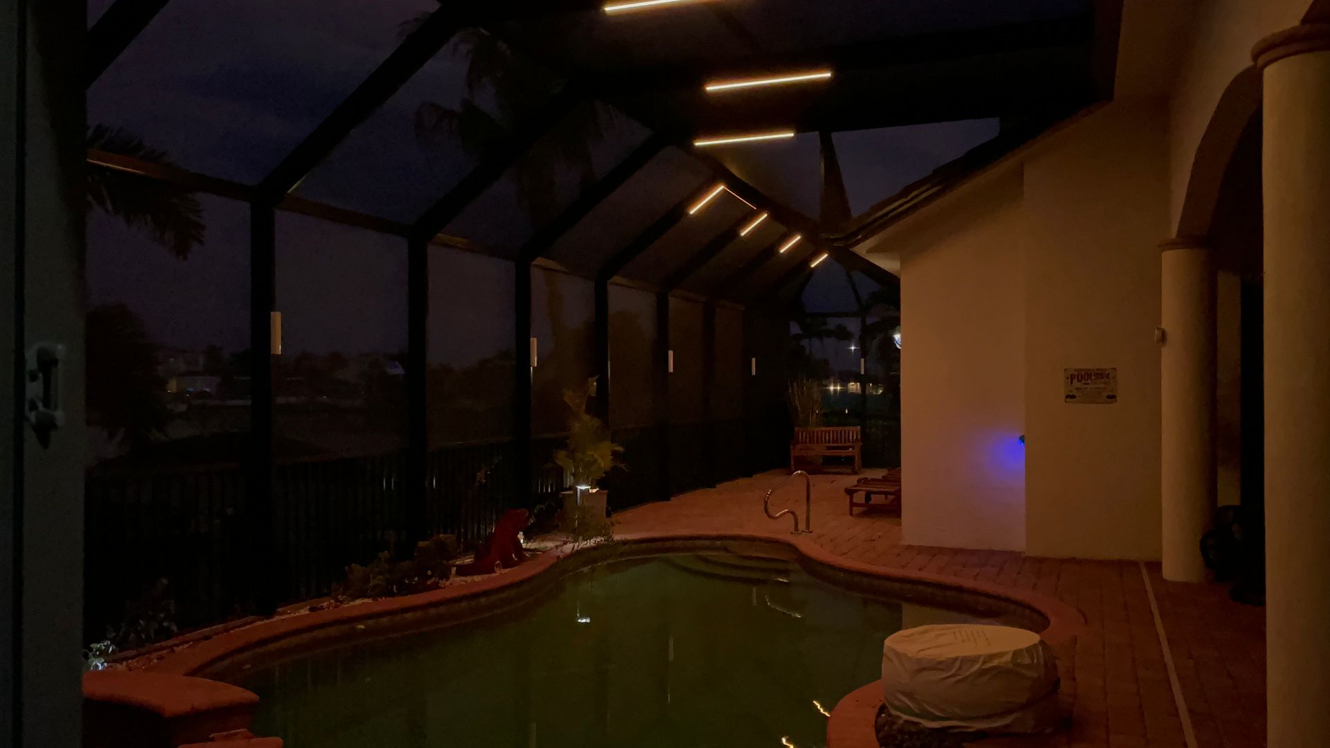 Pool area at dusk with overhead lighting, pool, and attached screened-in porch.