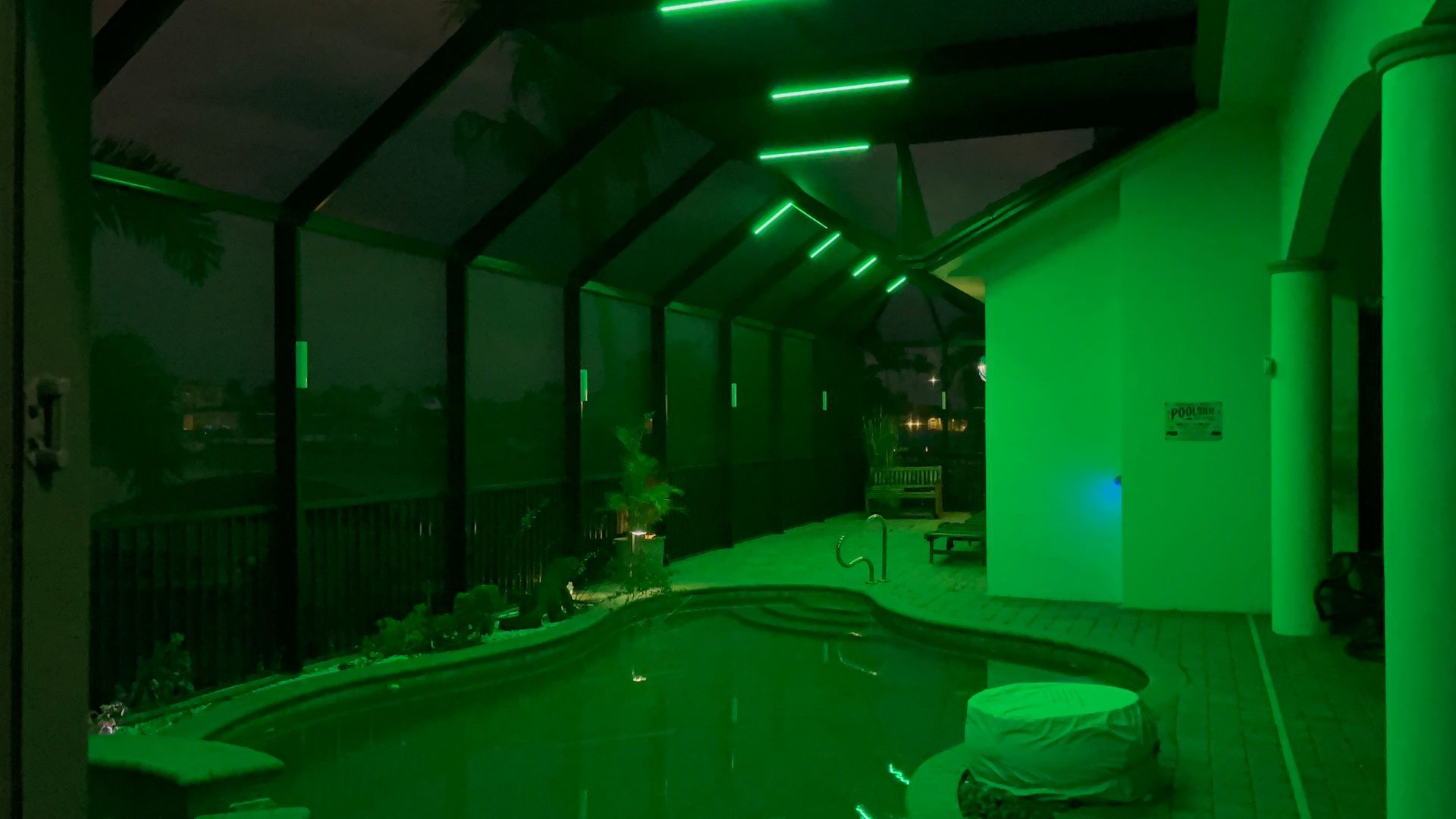 Pool area at night with green lights. Pool water and surrounding surfaces illuminated.