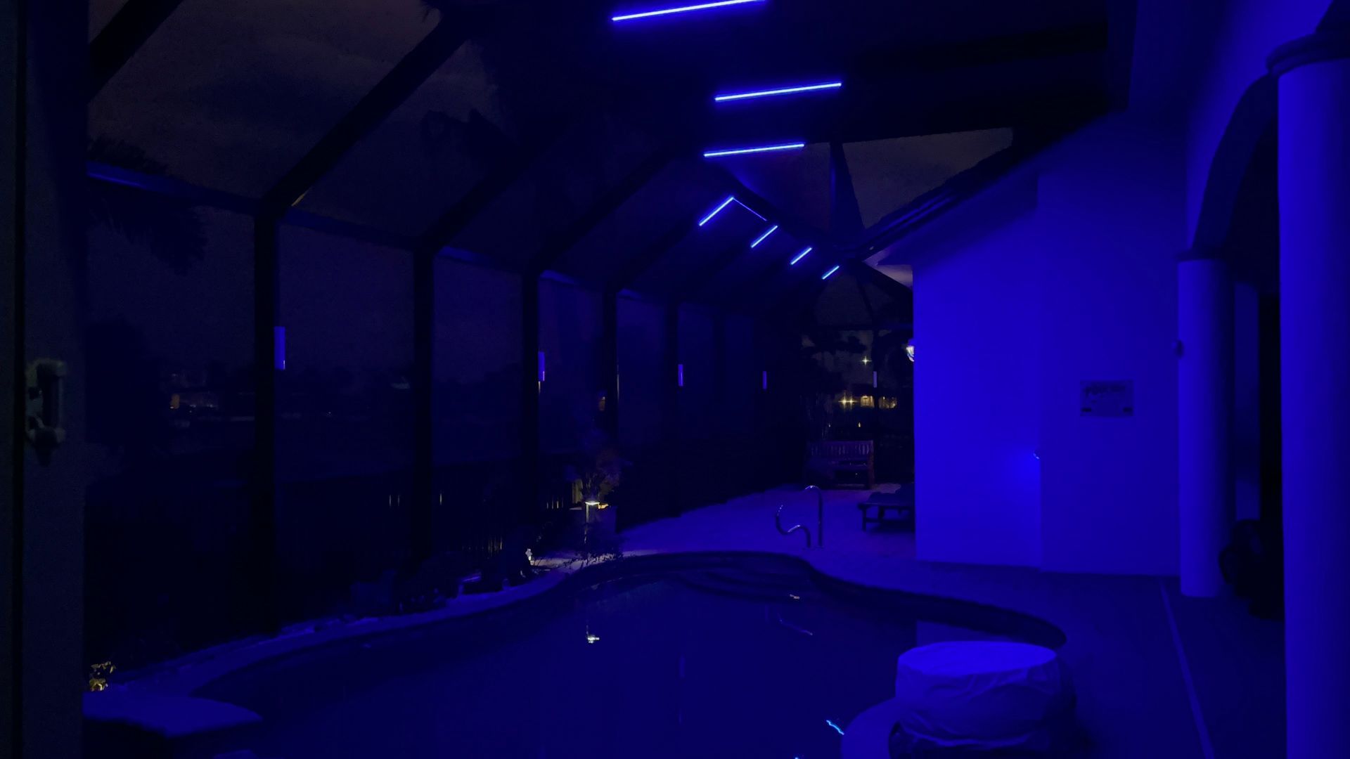 Indoor pool at night, lit with blue lights. Building and water reflections visible.