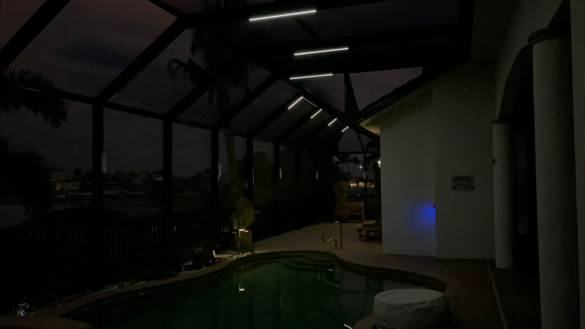 Pool area at night with enclosed screen ceiling. Blue and green lighting; dark.