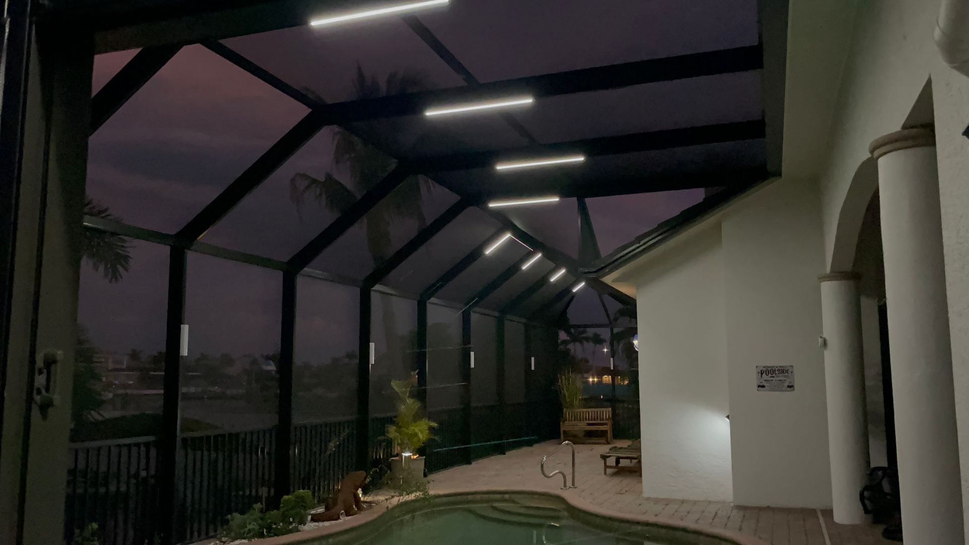A lit pool enclosure at dusk, with linear lights on the angled ceiling and pool in the foreground.