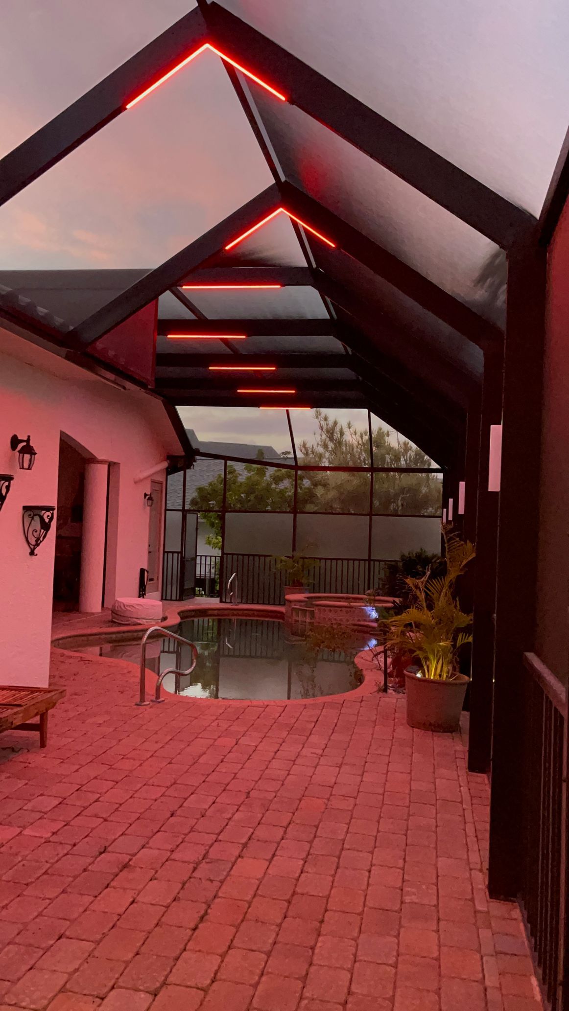Outdoor patio with red brick flooring, a pool, and black metal awning with red lights.