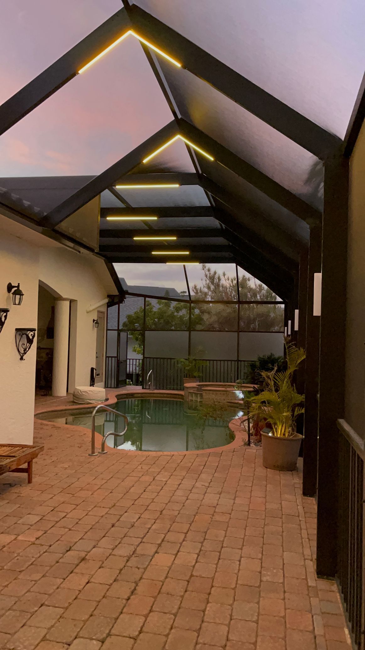 Pool area with brick patio under a covered structure, evening sky.