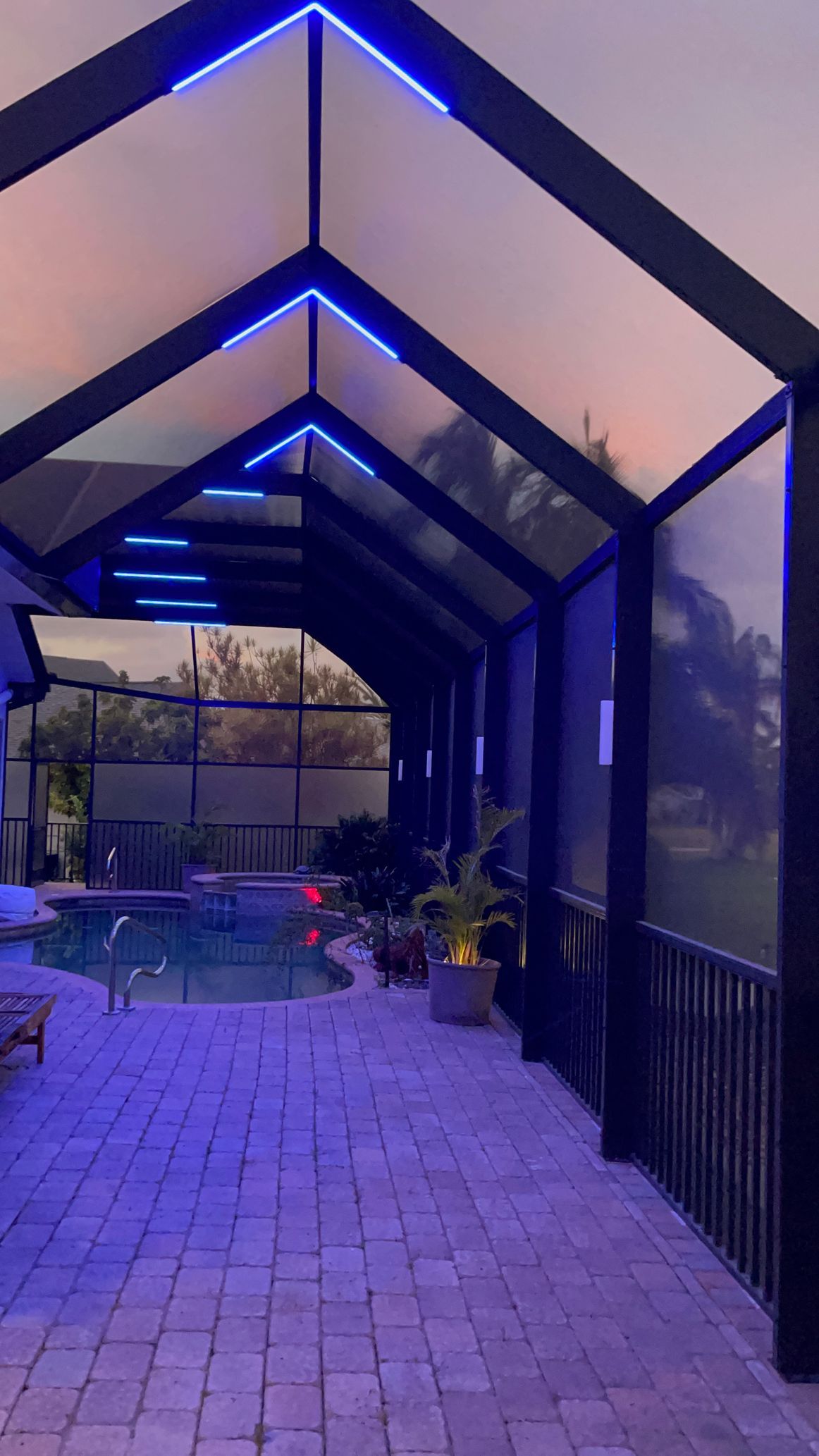 Patio with pool, enclosed by dark framed structure with blue LED lights. Brick floor.