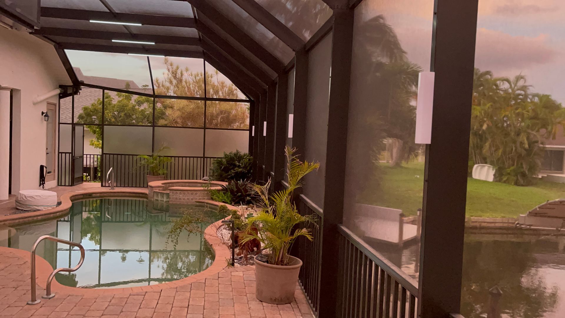 Pool area with a screened enclosure. Pool, hot tub, pond, and plants visible. Cloudy sky.