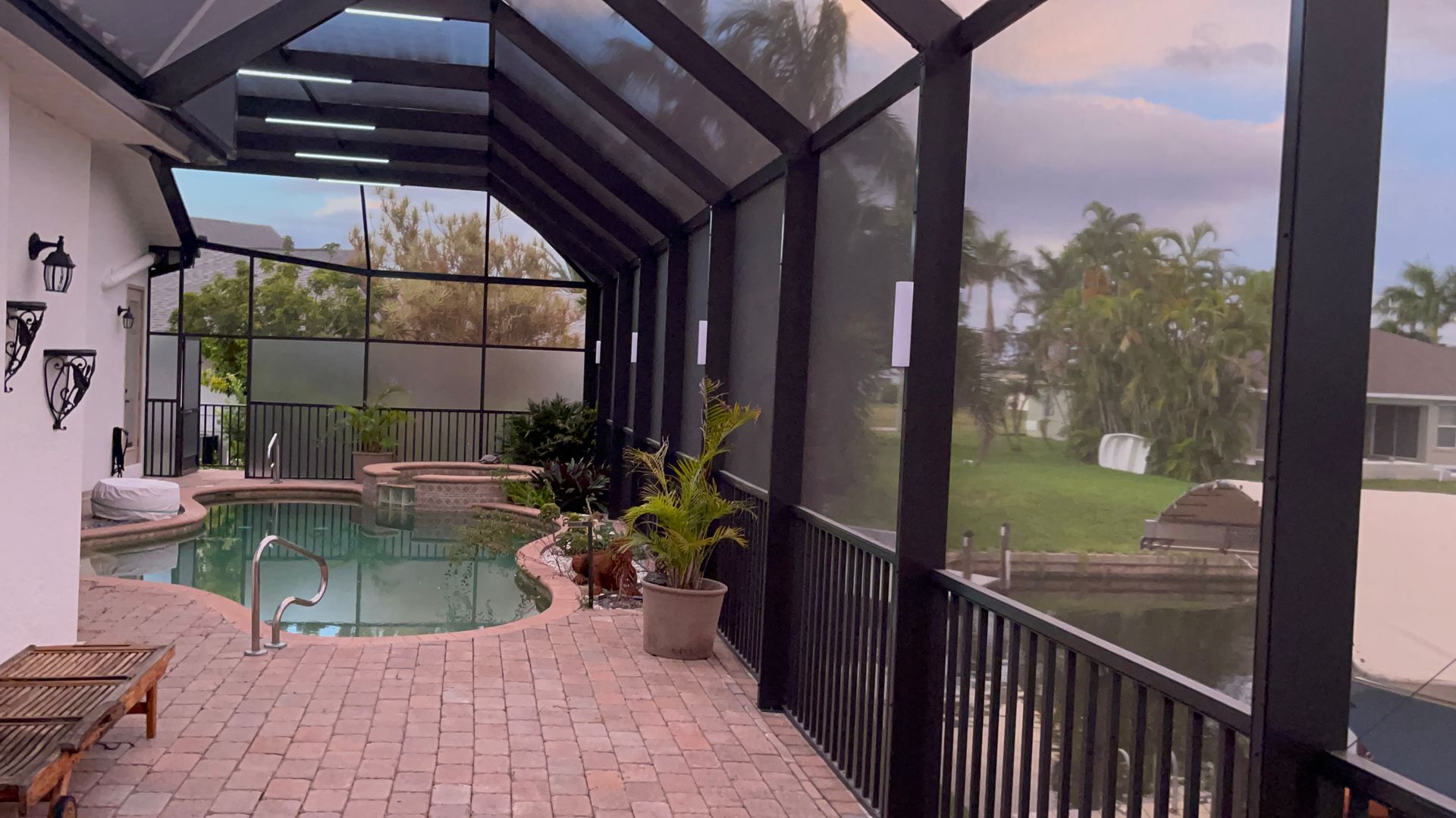 Poolside patio with pool, enclosed by a screen. A waterway and green yard are visible.