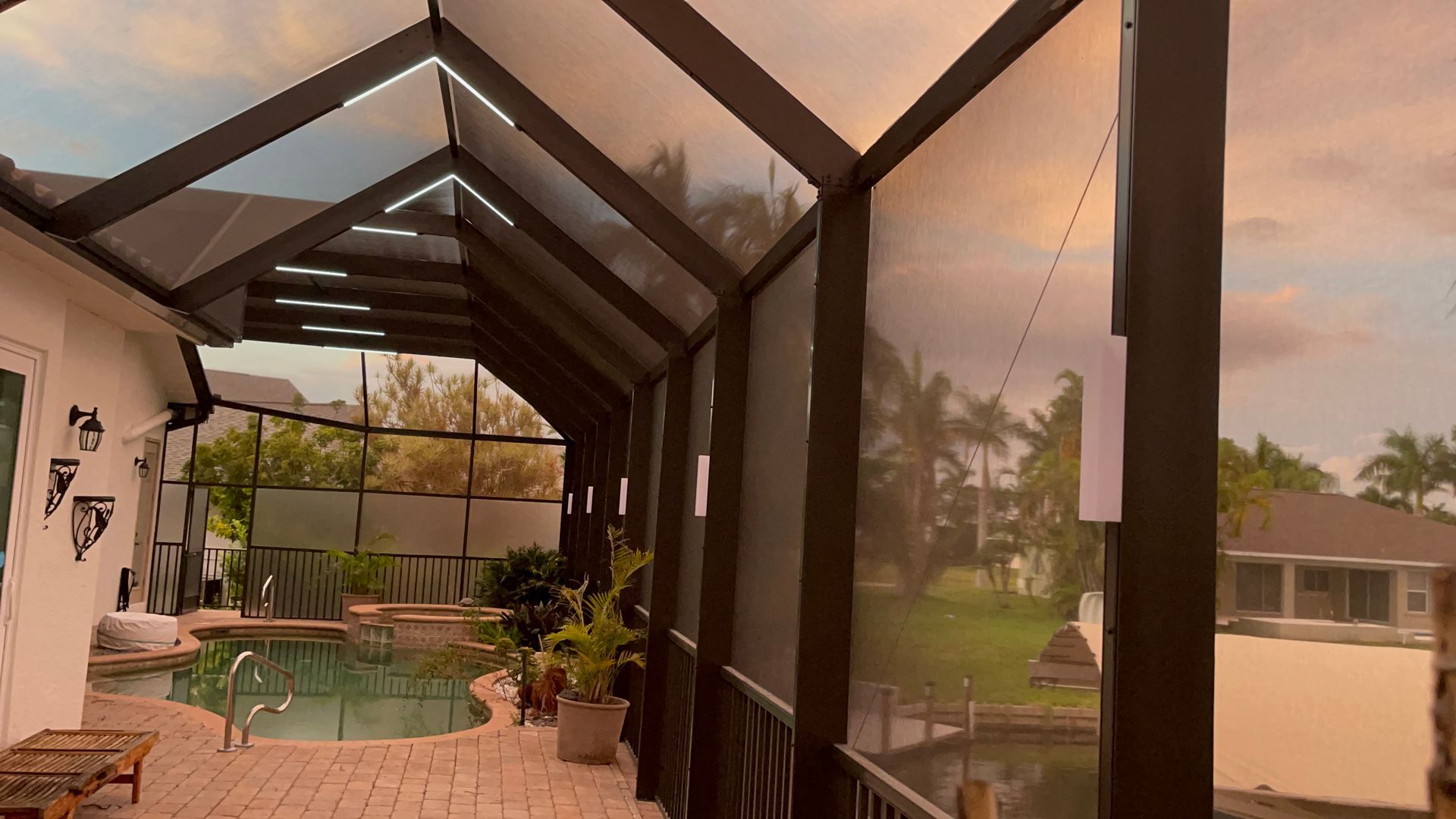 Screened patio with pool and canal view at sunset. Dark frame, light brown screen, and brick patio.
