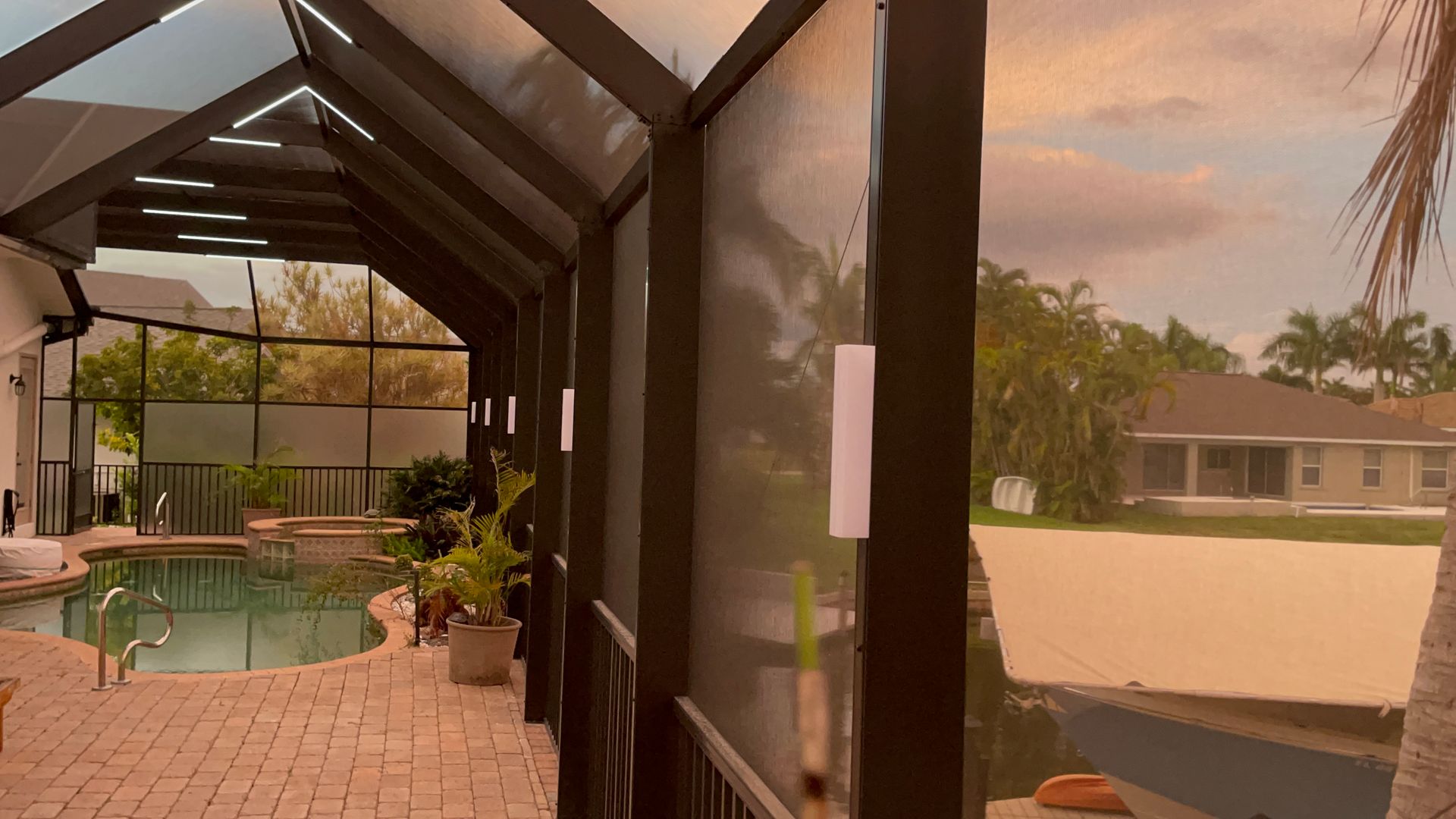 Pool area with screened-in porch, view of a sunset, and houses.