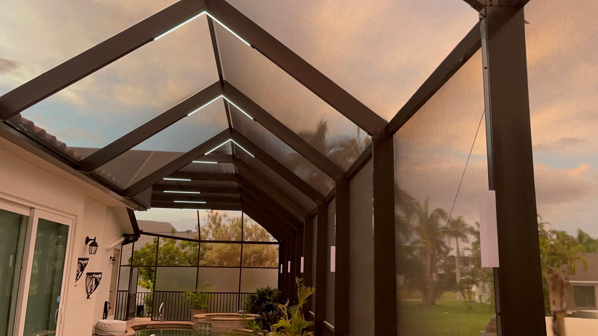 A screened-in patio with a dark roof and walls against a cloudy sky.