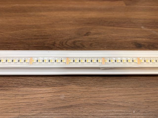 White LED light strip mounted on a wooden surface, with evenly spaced, illuminated LEDs.