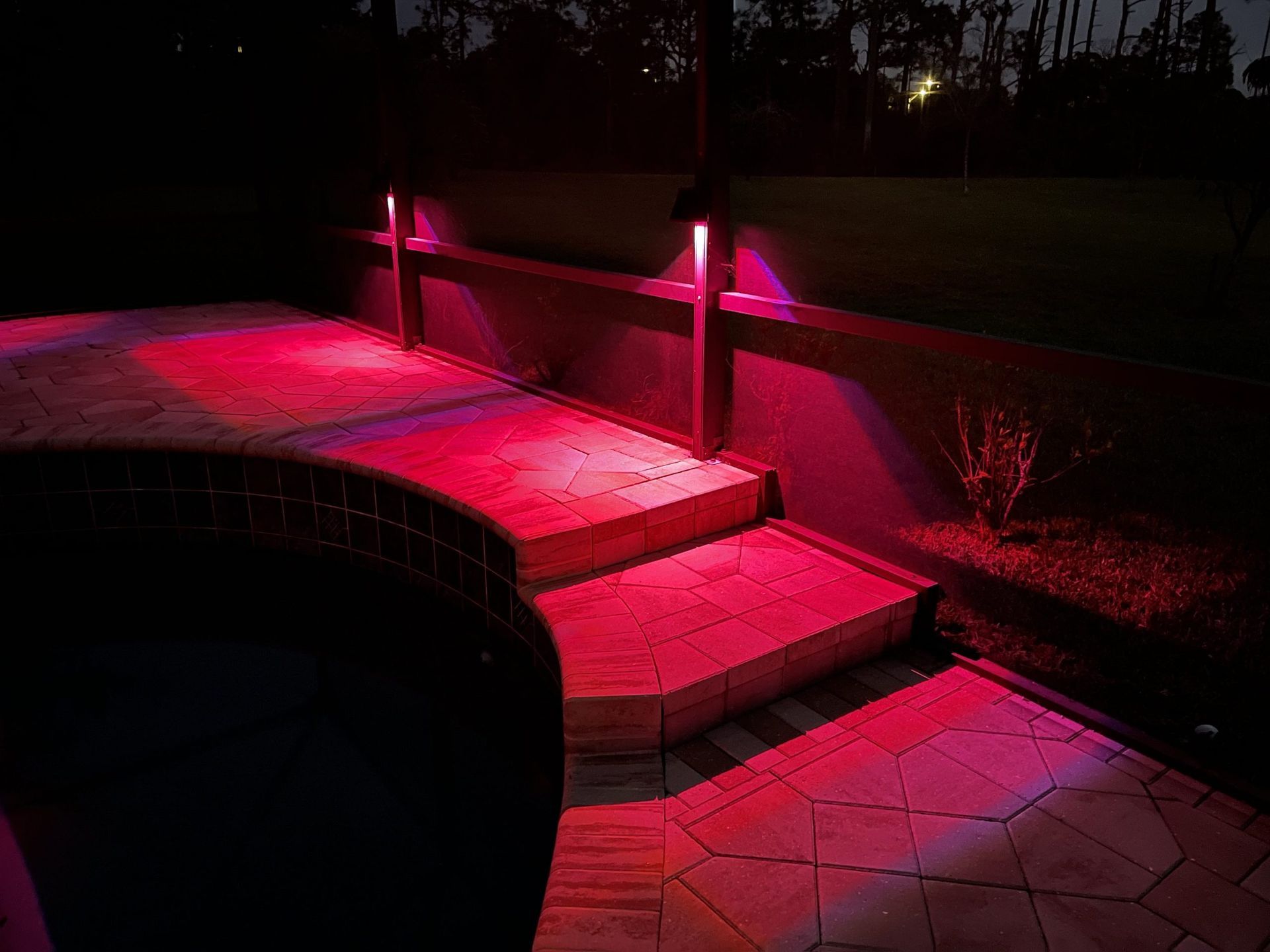 Red-lit outdoor steps and wall by a dark pool at night.
