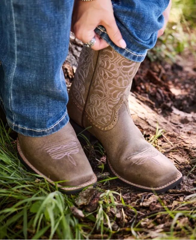Person rolling up blue jeans, revealing brown cowboy boots with intricate stitching.