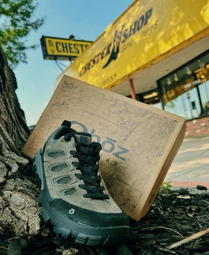 Gray hiking shoe and box leaning against a tree, with 