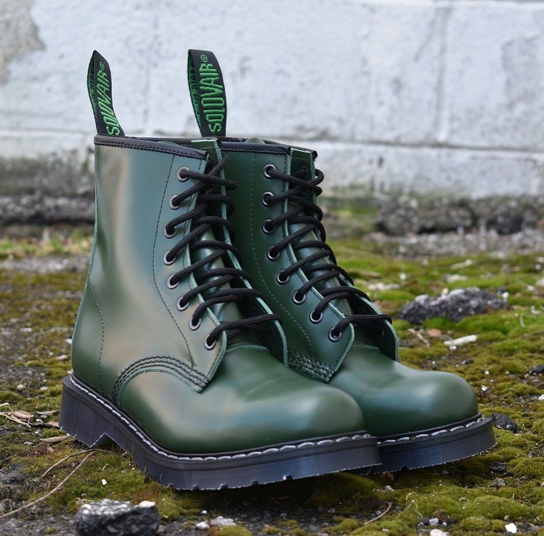Green combat boots with black laces, on a mossy surface.