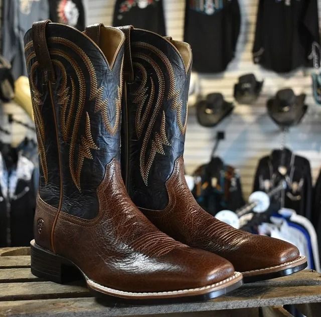 Brown and black leather cowboy boots with decorative stitching, displayed in a store.