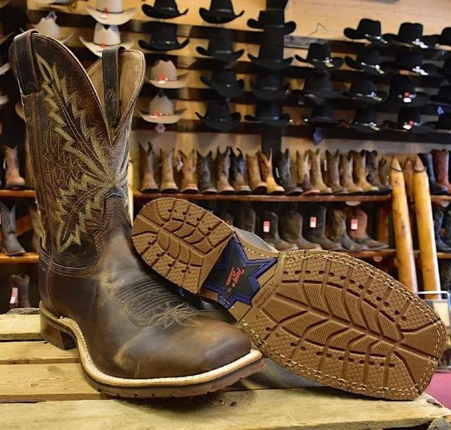 Brown cowboy boots with decorative stitching, set against a backdrop of more boots and hats in a store.