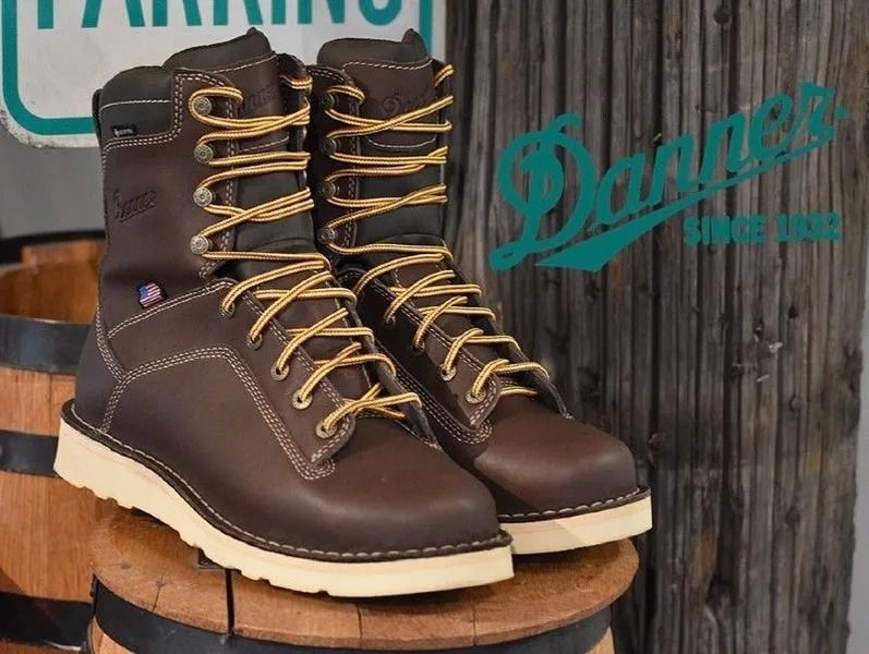 Brown leather Danner work boots with yellow laces and white soles on a wooden barrel.
