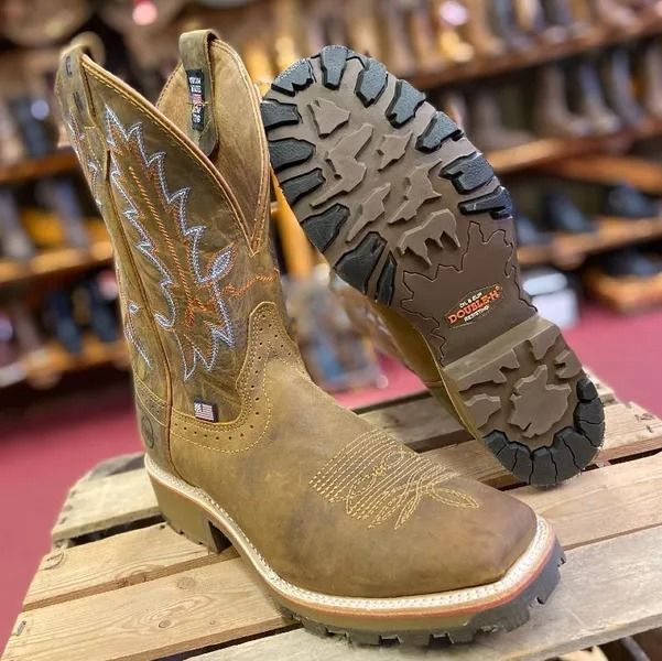 Tan leather work boots with detailed stitching and a rugged outsole, displayed on a wooden surface.