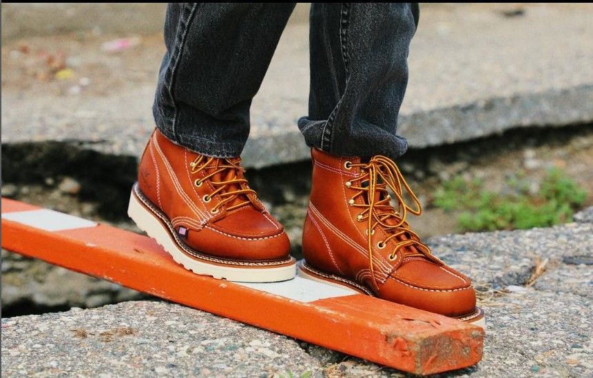 Brown work boots on an orange and white barrier, person in jeans.