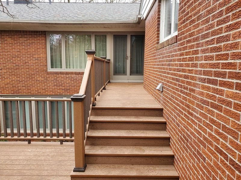 Brown steps lead up to a doorway on a brick building with a deck on the left.