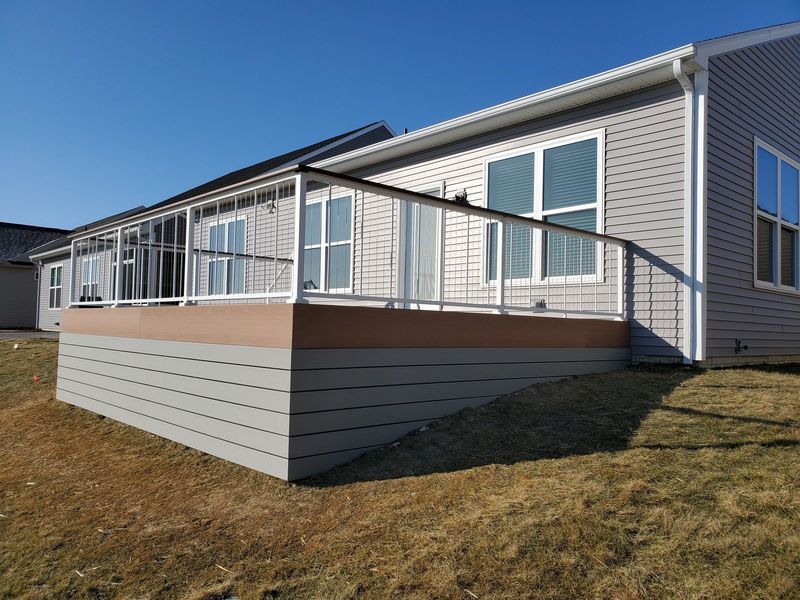 Composite deck with white railing attached to a light gray house.