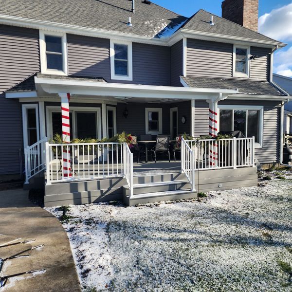Gray house with a front porch, white railing, and red and white striped columns; snow on the ground.