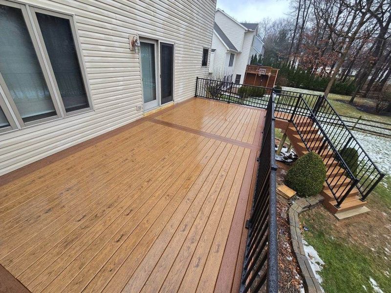 Wooden deck with black railing and steps; side of house visible. Winter scene with snow.