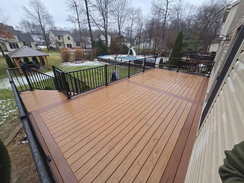 Brown composite deck with black railing and trim. Backyard setting with a pool and gazebo.